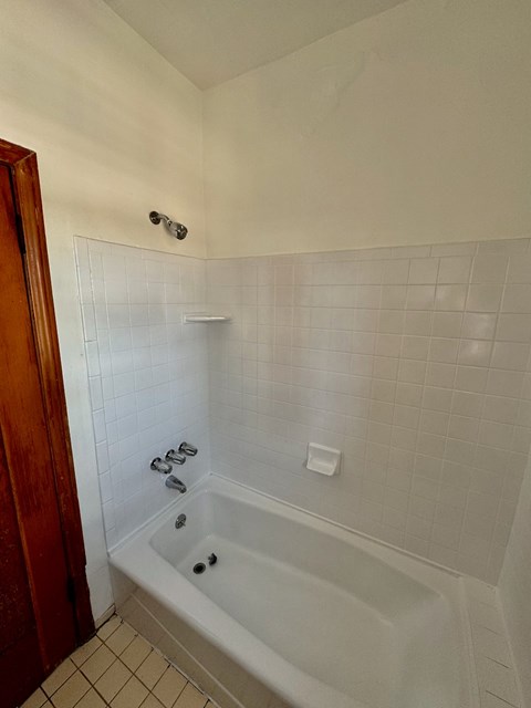 A white tiled bathroom with a white bathtub and a wooden door.