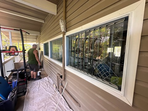 A man in a green shirt is working on a window on a house.