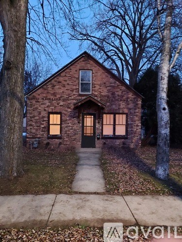 A house with a brick facade and a black door is surrounded by trees.