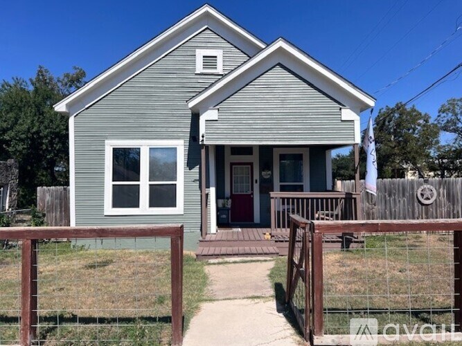 A grey house with a red door and a brown fence.