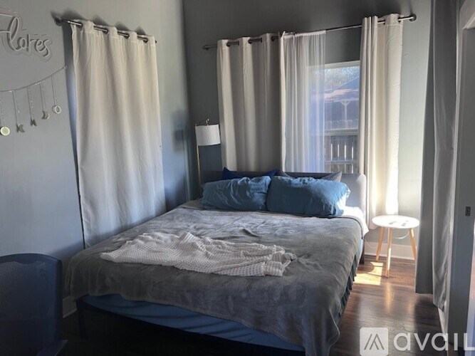 A bedroom with a bed, a chair, and a window with curtains.