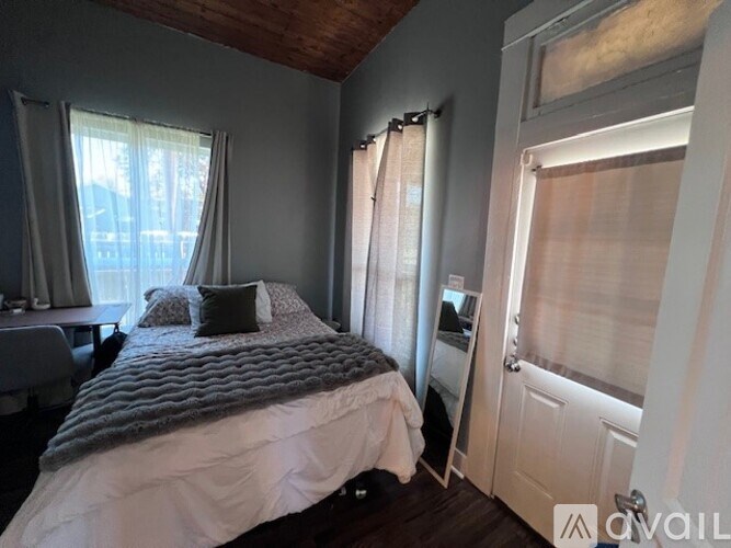 A bedroom with a bed, a window with curtains, and a door.
