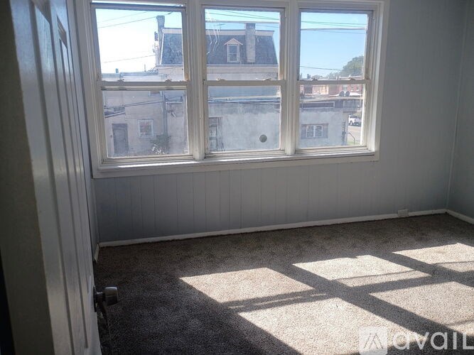 A room with a carpet floor and a window showing a view of a building.