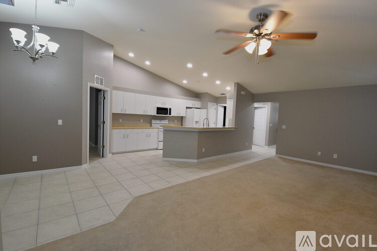 A spacious living room with a ceiling fan and a kitchen area in the background.
