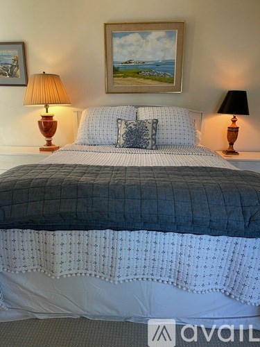 A bed with a grey and white comforter and a pillow with a blue and white pattern.