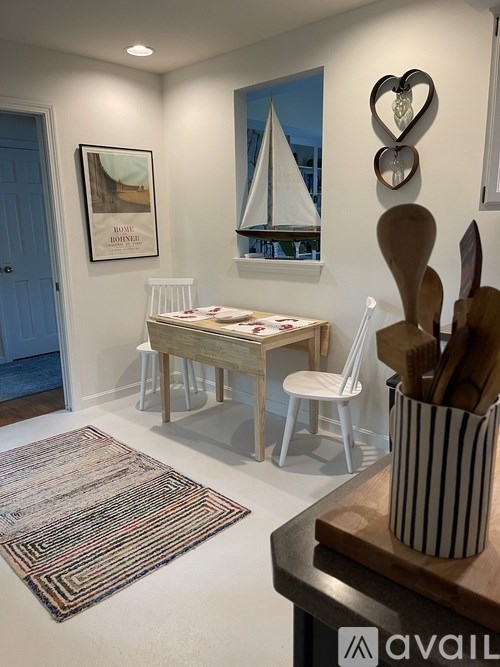 A kitchen with a white table and chairs, a rug, and a wooden cutting board with utensils on it.