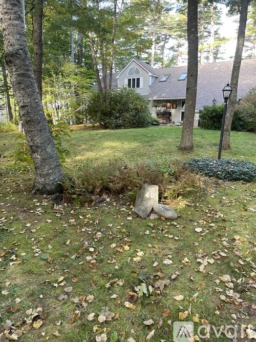 A stone statue is sitting in the middle of a grassy area with trees and a house in the background.