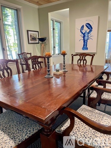 A wooden dining table with chairs and a painting of a lobster on the wall.