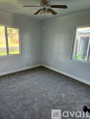 A room with a ceiling fan and two windows.