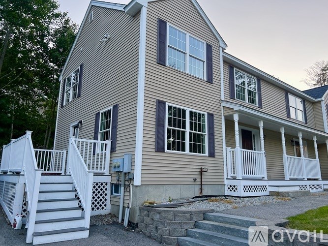 A two-story house with a white porch and a stone wall.
