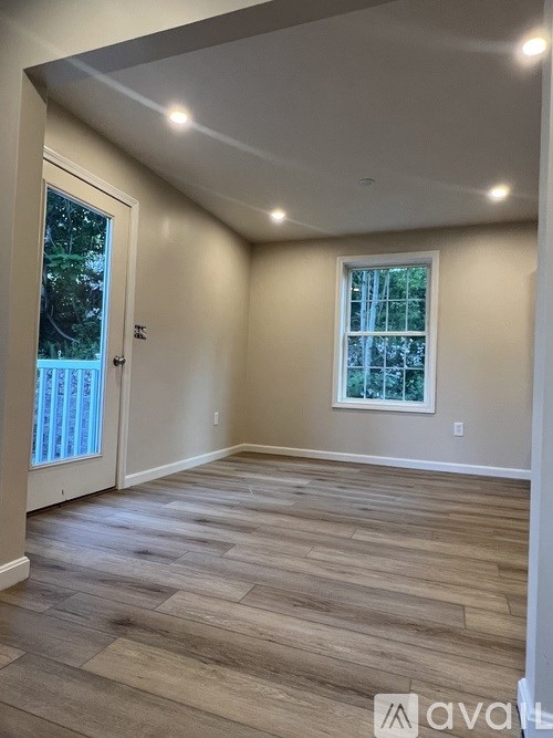 A room with wooden flooring and a window with a view of trees.