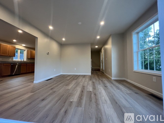 A spacious room with wooden flooring and a large window on the right side.