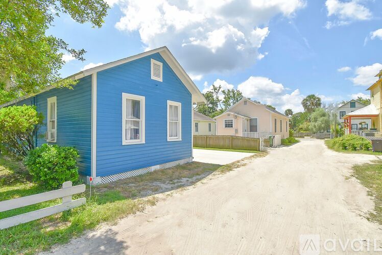 A blue house with a white fence and a dirt road in front.