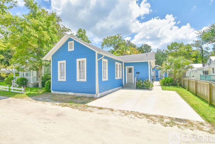 A blue house with a white fence and trees in the background.