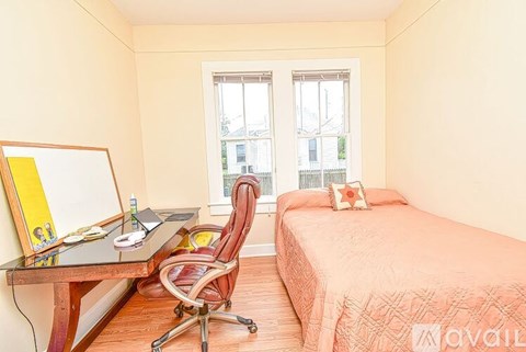 A bedroom with a bed, desk, chair, and window.