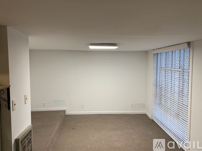 A spacious room with a carpeted floor and a window with blinds.