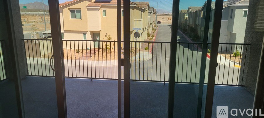 A balcony with a metal railing overlooks a courtyard with a few houses and a car.