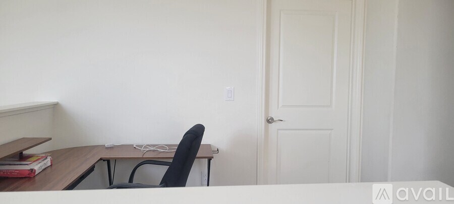 A black chair is in front of a desk with a white cord and a book on it.