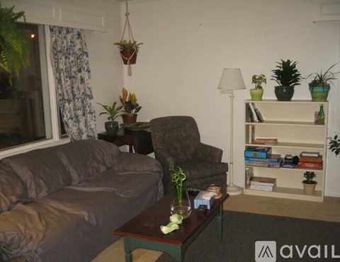 A living room with a grey couch, a table with a vase of flowers, and a bookshelf with various items.