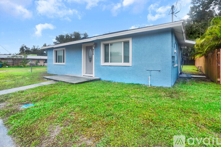 A blue house with a white door and windows is surrounded by a green lawn.