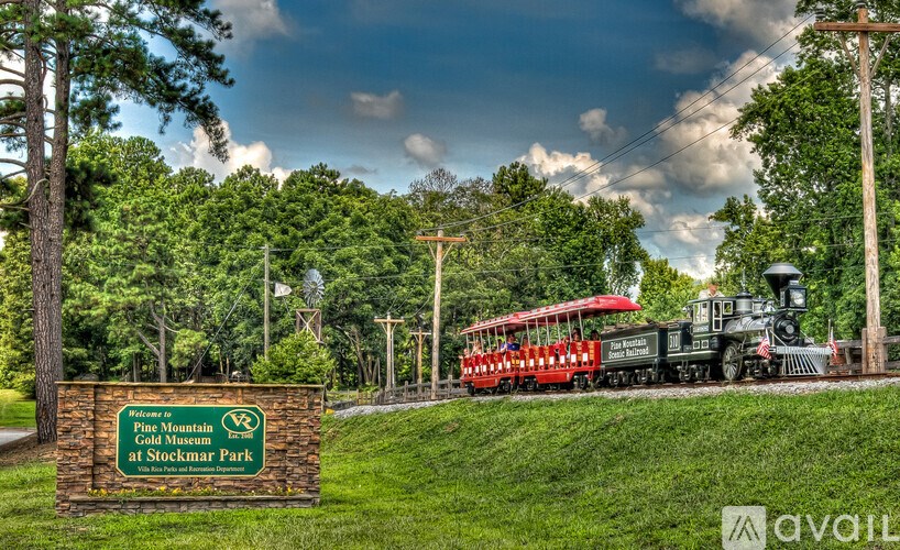 A sign for the Play Mountain Gold Museum at Stockmar Park with a train in the background.