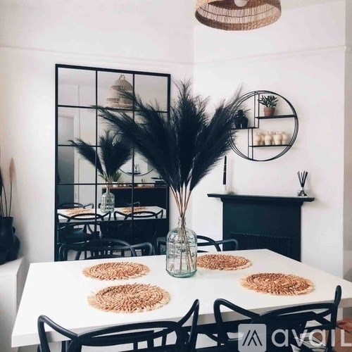 A dining table with a vase of feathers in the middle and a mirror on the wall.