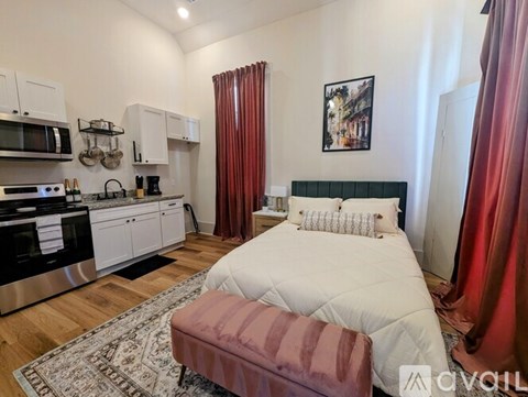 A bedroom with a bed, a bench, and a kitchen area with a microwave and oven.