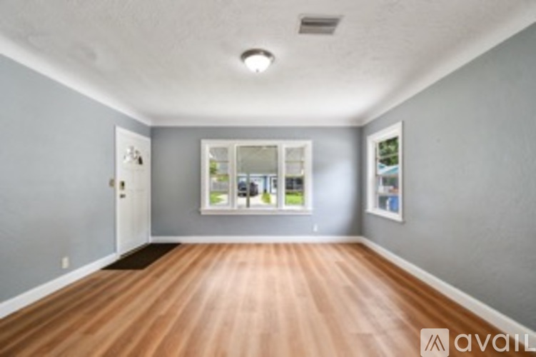 A room with wooden floors and a window showing a view of trees.