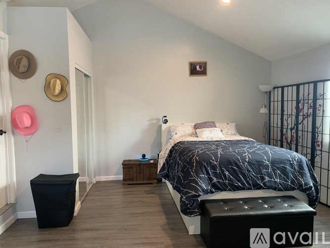 A bedroom with a bed, nightstand, and a black ottoman.