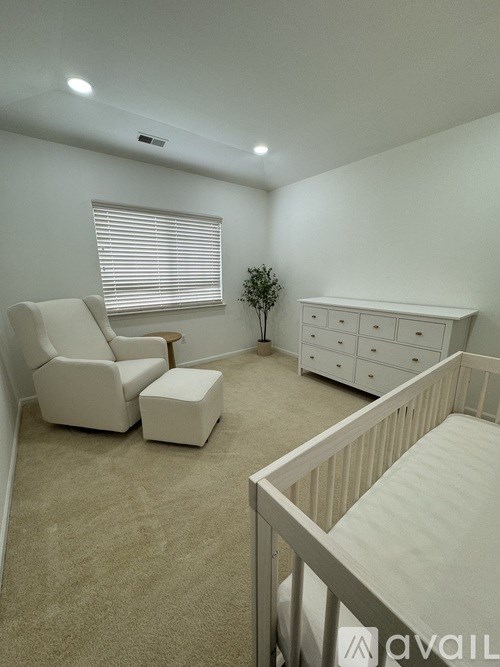 A baby room with a crib, chair, and a small tree.