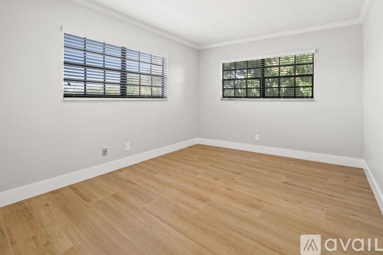 A room with wooden flooring and two windows.