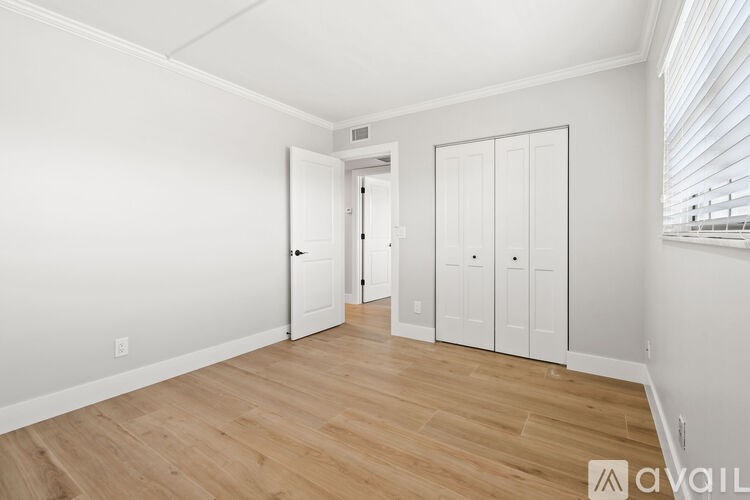 A room with white walls and wooden flooring, featuring a white door and a white wardrobe.
