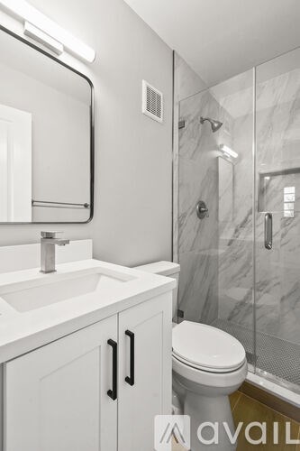A white bathroom with a toilet, sink, mirror and shower.