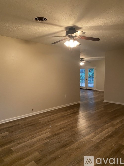 A room with a ceiling fan and light fixture, and a wooden floor.