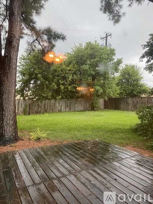 A wooden deck in the foreground with a backyard and a fence.