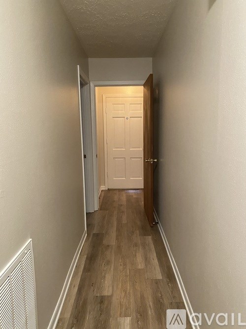 A hallway with a white door and wooden floors.