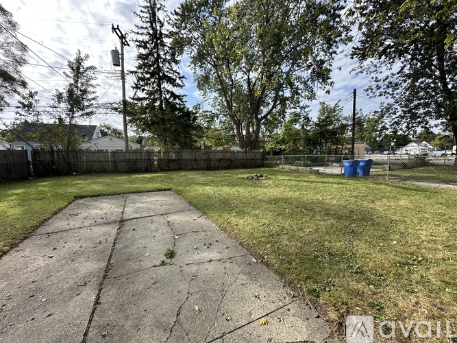 A backyard with a concrete slab and a blue trash can.
