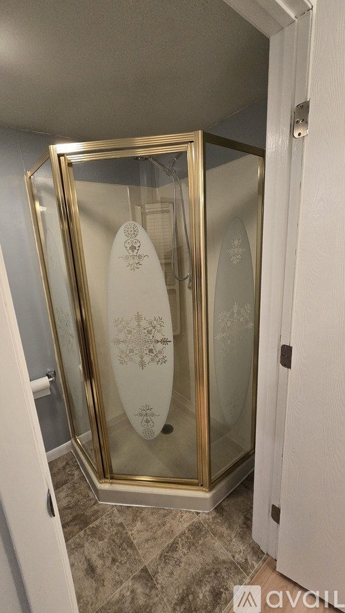 A gold framed glass shower door with a white surfboard design.