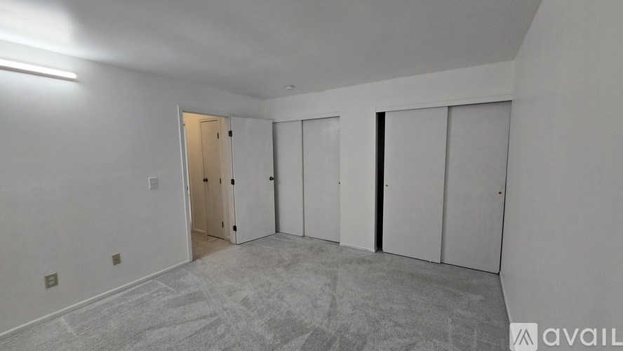 A room with a carpeted floor and white walls, featuring a door, a wardrobe, and a wall-mounted shelf.