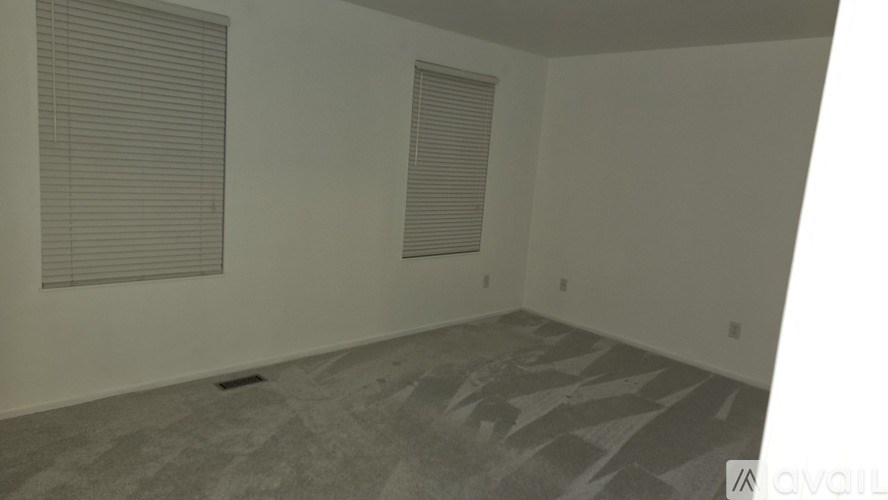A room with a carpeted floor and two windows with blinds.