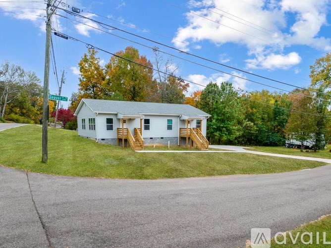 A house with a white exterior and a grey roof is surrounded by green grass and trees.