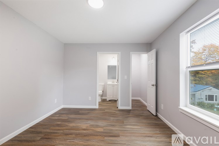 A room with wooden flooring and white walls, with a window showing a tree outside.
