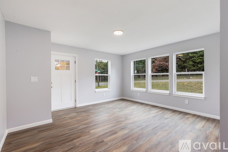 A spacious room with wooden flooring and three windows showing outdoor views.