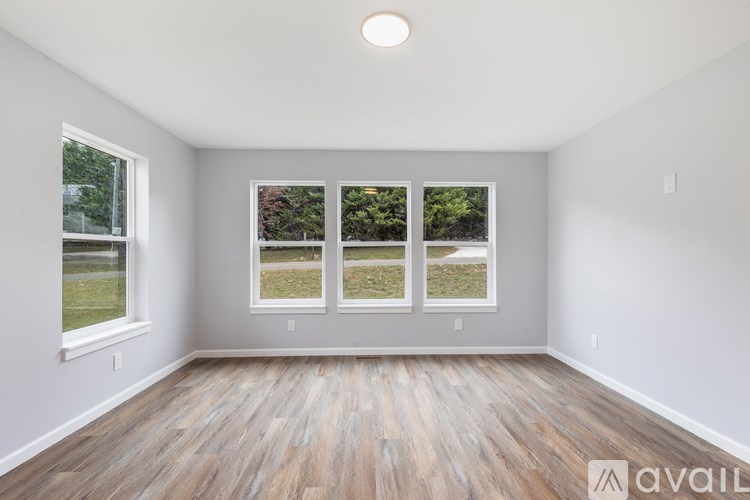 A room with wooden floors and three windows showing greenery outside.