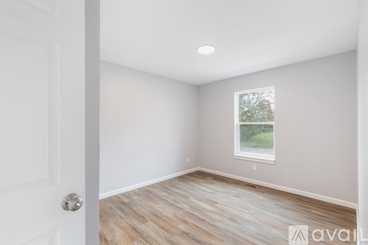 A room with a white door and a window with a view of trees.