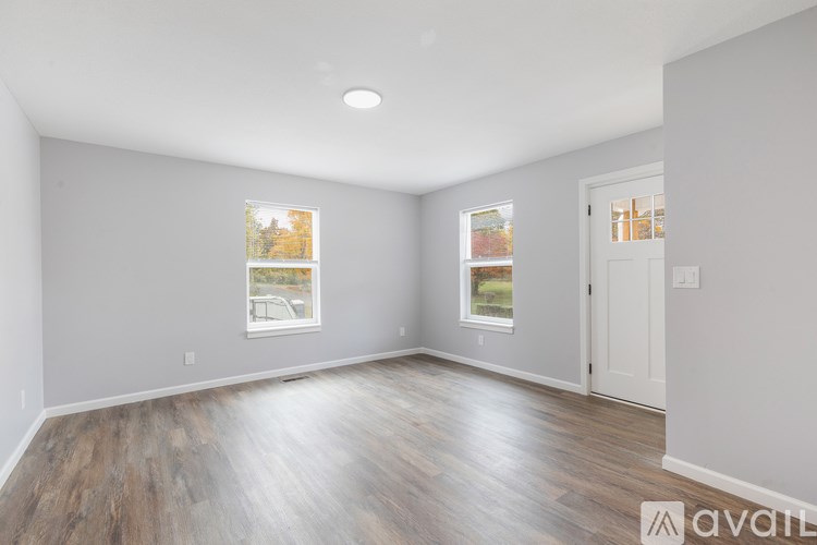 A spacious room with wooden flooring and two windows.