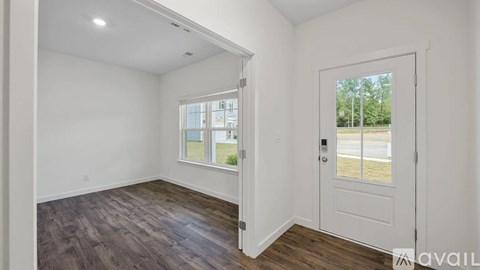 A room with a white door and a window with a view of a building and trees outside.