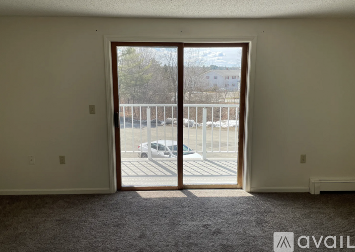 A room with a carpeted floor and a large open door leading to a parking lot.