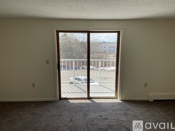A room with a carpeted floor and a large open door leading to a parking lot.