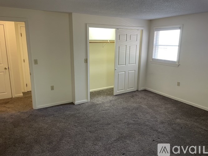 A room with a carpeted floor, a white door, and a window.